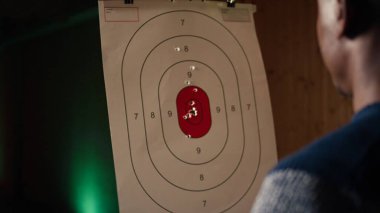 Atış poligonu müşterisi tabancayla ateş ediyor. Hedefe ateş edip etmediğini kontrol ediyor. Atış poligonunda silah kullanmayı öğrenen, hedeflerin görüntülerini analiz eden, kamera A.