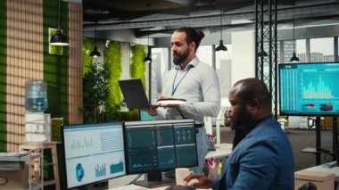 Erkek takım lideri, ortak çalışma alanındaki bir dizüstü bilgisayardaki analizleri izliyor ve iş verimliliği için günlük görevleri yerine getiriyor. Performans ölçümlerini ve gelişim için diğer anlayışları kullanarak. Kamera A.