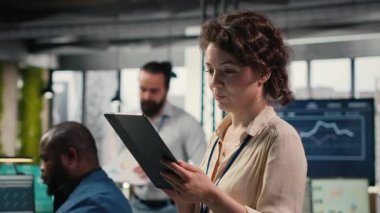 Yeni bir vizyon oluşturmak için dijital araçlar kullanan kadın ofis yöneticisi, modern ofis ortamında hedeflere ulaşmak için tabletteki performans veri içgörülerini gözden geçiriyor. Kamera B.