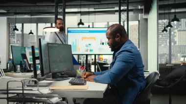 Afrikalı Amerikalı analist bir ders kitabına büyüme stratejisi notları yazıyor. İş ofisinde öngörüler ve finansal verilerle çalışıyor. Danışman operasyonel başarı ve verimliliği garanti ediyor. Kamera A.