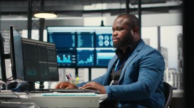 Afrika kökenli Amerikalı erkek, finansal veri tahminlerini bilgisayarda analiz ediyor. Şirket amaçlarıyla uyum sağlamak için yenilikçi iş çözümleri geliştiriyor. Profesyonel çevre. Kamera B.