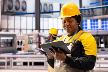 Tabletli profesyonel mühendis endüstriyel üretim tesisinde otomatikleştirilmiş makinelerin verimliliğini arttırıyor. Siyah kadın endüstrisi 4.0 uzman akıllı fabrikada robot silah üretimini denetliyor..