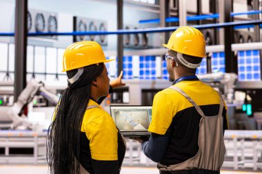 İki endüstri 4.0 mühendisi üretim hattı yeniliklerini izliyor ve dizüstü bilgisayardaki dijital kontrolleri analiz ediyor. Akıllı üretim otomatikler ve otomatikler ile otomatikleştirilmiş fabrikalarda verimlilik entegre edilir.