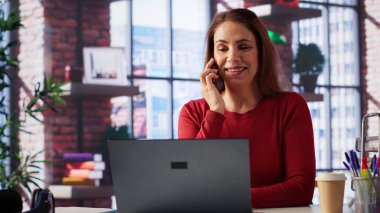 Ev ofisinin çatı katında bilgisayarla çalışırken cep telefonuyla konuşan odaklanmış bir kadın. Görevleri çözmek için iletişim becerileri ve yaratıcılığı kullanarak çağrılarla, toplantılarla ve soruşturmalarla uğraşıyor. Kamera A.