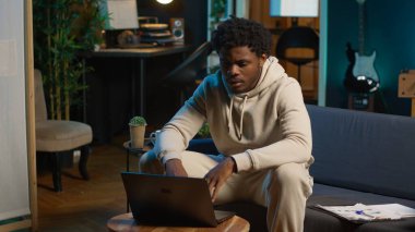 Hırslı siyahi adam rahat oturma odasında tek başına yeni bir dil öğreniyor. İnternette çalışma platformları ve açıklamalar arıyor. Yetişkin bilgisayarında dil öğrenme yazılımı kullanıyor. Kamera A.