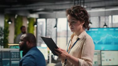 Kadın iş danışmanı, çalışma verimliliği için etkin yönetim ve stratejik planlama becerileri gösteren aylık raporlar oluşturmak üzere tablet üzerindeki çizelgeleri ve simgeleri inceliyor. Kamera B.