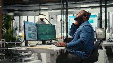 Boynu tutulmuş, sırt ağrısı olan, kaslarını esneten, iş yaparken kötü duruşunu düzelten Afrikalı Amerikalı bir adam. Organizasyonun başarısına odaklan. Kamera A.