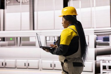 Endüstriyel fabrikada, kadın teknisyen otomatik üretim hattını denetlemek için dijital aletler kullanıyor. Akıllı üretim sistemi, geliştirilmiş üretim için robot kollarını ve taşıyıcı bantlarını sorunsuzca entegre eder