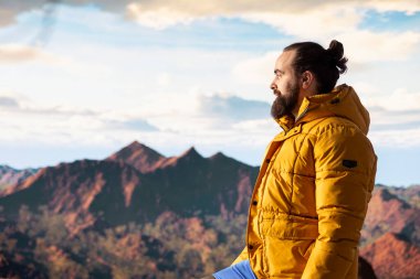 Yürüyüşçü, vahşi doğada yürümenin zorluğunu kucaklıyor, panoramik dağ manzarasının tadını çıkararak, gücün ve açık hava macerasının ödüllerini anımsatıyor. Macera Avcısı.