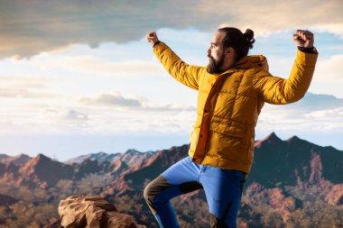 Tatmin olmuş maceracı, yüksek bir dağın tepesinde durur destansı manzarayı seyreder ve yürüyüş başarısıyla gurur duyar. Güçlü neşeli yürüyüşçü, tatminkar deneyimi hissediyor.