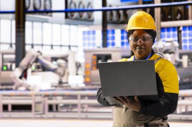 Yenilenebilir enerji tesisinde gelişmiş teknolojiyle çalışan siyah kadın mühendis. Dizüstü bilgisayar tutan ve güneş panellerini ve çevre dostu ekipmanları izleyen Afrikalı Amerikalı kadın..