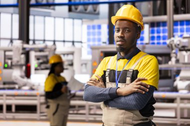 Otomatik imalat fabrikasındaki erkek teknisyen ileri üretim hattının önünde duruyor. Robotik otomasyon ve dijital sistemlerle. Afrikalı Amerikalı adam akıllı fabrikanın bakımını denetliyor..