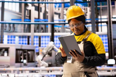 Akıllı imalat danışmanı tabletine sistem kontrolü yapıyor. Afrika kökenli Amerikalı kadın mühendis, üretim tesislerindeki teknolojik gelişmeleri yönlendirmek için dijital araçlar kullanıyor..