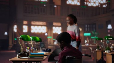 Engelli erkek öğrenci üniversite kütüphanesinde sınav hazırlıkları yapıyor, kız da onun masaya ulaşmasına yardım ediyor. Tekerlekli sandalye kullanıcısı burs için akademik evrak işleriyle uğraşıyor. Kamera A.