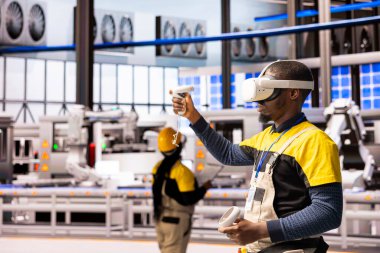 Otomatik fabrikadaki profesyonel mühendis, endüstriyel sanayi işletmeleri için yenilikçi yazılımı test etmek amacıyla VR kulaklık takıyor. Siyah erkek teknisyen sanayi 4.0 eğitimi için artırılmış gerçekliği kullanıyor..