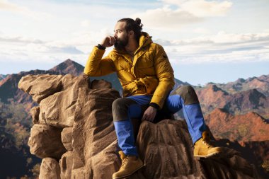 Kararlı gezgin, panoramik manzaranın macera ve kişisel gelişimi temsil ettiği bir dağ zirvesinin yalnızlığının tadını çıkarıyor. Açık hava teçhizatıyla yürüyüşçü rüzgarlı dağın tepesinde üşüyor..
