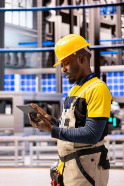 Afro-Amerikan mühendis endüstriyel otomasyon yazılımını sektör 4.0 tesisinde izliyor. Profesyonel teknisyen akıllı üretim tesisinde otomatikleştirilmiş fabrika işlemlerini optimize etmek için tablet kullanır.