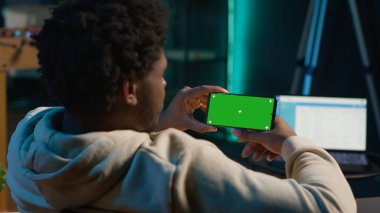 Afrika kökenli Amerikalı erkek serbest çalışan elinde sahte krom ekran olan, kanepesinde neon ışıklarının ve akıllı televizyon düzeneğinin yanında dinlenen bir cihaz. Genç yetişkin evinde mutlu hissediyor. Kamera A.