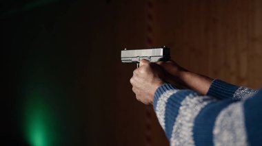 Atış galerisi müşterisi, kağıt hedefleri vurmak için tabanca kullanıyor. Kapalı alandaki atış poligonu tesisinde güvenlik ekipmanı takan birini yakından çek. Boğa avcılarını vur, silah kullanmaktan zevk al, kamera A.