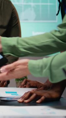 Dikey Video Çoklu Etnik Öngörü Ekibi önemli toplantı sırasında rapor dosyalarını gözden geçiriyor, proje gündemini güncelliyor ve mesai bitiminden sonra hissedarlarla iş geliştirme konusunu tartışıyor. Kamera.