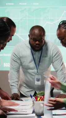 Dikey Video çok ırklı ekip dosya değiş tokuşu ve tahmin şemalarını gözden geçirip sessiz bir ofis alanında toplanıyor. Hissedarlar için anahtar proje güncellemelerini hazırlamak için saatler sonra işbirliği