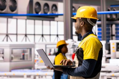 Erkek mühendis, akıllı üretim fabrikasındaki iş akışını optimize etmek için otomasyon ve dijital araçlar kullanan yenilikçi makinelerin üretimini izliyor. Sanayi 4.0 uzmanı montaj hattı bakımını denetliyor.