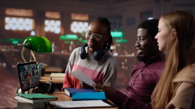 Çeşitli öğrencilerden oluşan bir grup, kampüs kütüphanesindeki uzak sınıf seminerine katılmak üzere çevrimiçi kurslara katılıyor. Gençler akademik hocadan notlar alıyorlar. Kamera A.