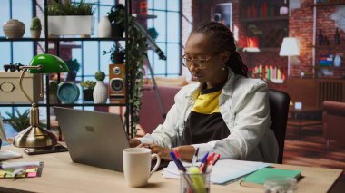 Ofisteki telgraf işçisi dizüstü bilgisayarla çalışırken esniyor ve yorgun hissediyor. Yeşim Afro-Amerikan uzaktan kumandalı çalışan rahatlayan kaslar, not defterindeki görevleri çözen, kamera A