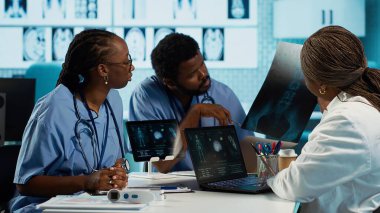 Kabinede bir sağlık ekibine liderlik eden Afrikalı Amerikalı pratisyen, MRI görüntüleme sonuçlarını analiz ediyor ve doğru teşhis ve etkili tedavi sağlıyor. Tıbbi tesis. Kamera A.
