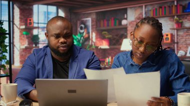 Siyahi insanların her ikisi de görev yönetimi için bilgisayarlarında online araçlar kullanarak belirlenen ofislerinde çalışırlar. Konforlu evlerinden işlemleri verimli bir şekilde tamamlıyorlar. Kamera A.