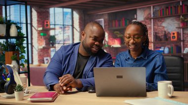 Siyah adam ve kadın rahat dairelerinde çalışıyorlar. Bilgisayarda dijital pazarlama stratejilerini tartışıyorlar. Online aletlere işaret ediyorlar. Uzaktan bağımsız yolculuklarında birbirlerine destek oluyorlar. Kamera A.