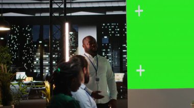 Siyahi erkek yönetici, çok uluslu bir şirketin yönetim kurulunda krom anahtar ekranlı bir toplantıya ev sahipliği yapıyor. Önerileri değerlendiriyor ve iş geleceği için kararlar alıyor. Kamera B.