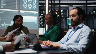 Erkek muhasebe müdürü tüm aylık giderleri gözden geçiriyor, iş ekibiyle gece vakti yaptığı toplantıda dizüstü bilgisayardaki veri güncellemelerini inceliyor. Mesai sonrası sahnesi. Kamera A.