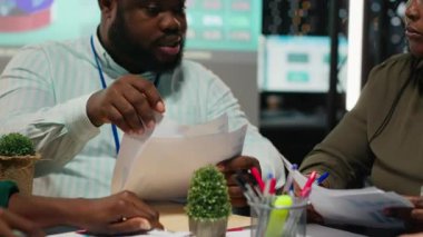 Proje sorunlarını çözmek için çözümler sunmak amacıyla bilgi grafiklerini gözden geçiren çok ırklı ekip, son teslim tarihinden önce görevleri tamamlamak için saatler sonra çalışıyor. Sorun çözme toplantısına katılan analistler. Kamera B.