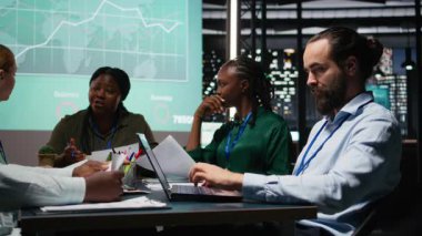 Çeşitli analistlerden oluşan ekip, mesai saatleri dışında yapılan toplantılarda yıllık veri raporlarını inceleyerek, üretkenliği sağlamak için iç iletişimi geliştirdiler. Girişim geliştirme planları üzerinde çalışıyorum. Kamera A.