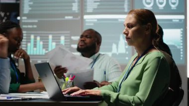 Çeşitli çalışanlar, gece toplantı sırasında hedeflerle uyumlu bir iş stratejisi geliştiriyor, pazar dinamikleri ve tahminleri inceliyor. Mesai sonrası brifing. Kamera B.