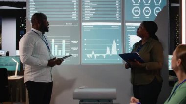 Siyahi iş danışmanları, mesai sonrası brifing sırasında aylık veri içgörülerini açıklıyorlar, mali ayrıntılara giriyorlar ve karanlık ofisteki yönetim kurulu üyeleriyle güncellemeler yapıyorlar. Kamera A.