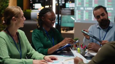 İş adamları toplantı odasındaki dosya raporlarının mali verilerini inceleyerek sunuma hazırlanıyorlar. Bilgi alışverişi ve yönetim için hava durumu güncellemeleri. Kamera B.
