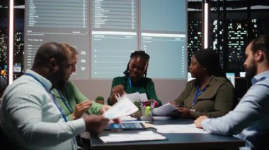 Çeşitli iş adamlarının gece geç saatlerde sessiz bir strateji odasında şirket hedeflerini tahmin etmek için raporlarını ve görüşlerini paylaştıklarını. Finans projeleri işbirliği. Kamera A.