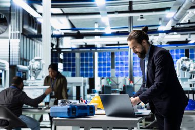 Yüksek teknolojili bir fabrikada güneş paneli mühendisi denetleme yapıyor, kalite kontrol ölçümleri yapıyor. Gelişim için endüstriyel operasyonları güvence altına alan profesyonel danışman.