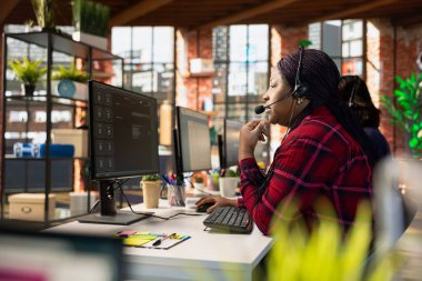 Ofis masasındaki merkezi ara. Müşteri etkileşimini arttırmak ve soruşturmaları etkili bir şekilde çözmek için yapay zekayı kullan. Afro-Amerikan müşteri hizmetleri çalışanı yapay zeka iletişim teknolojileri kullanıyor.