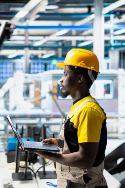 Mühendis güneş paneli yenilenebilir enerji konfigürasyonlarını inceleyerek güneş pillerinin üretim hattı üzerinde çalışıyor. Afrika kökenli Amerikalı erkek işçi CAD endüstriyel yazılımı kullanıyor.