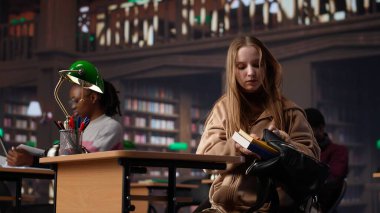 Bayan üniversite öğrencisi yeni bir ders için ayrıntılı notlar okuyup yazıyor, üniversitedeki kütüphane ortamında verilecek bir ders için siyaset bilimi okuyor. Kız danışmanlık veritabanı. Kamera A.