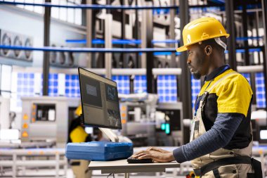 Siyah erkek teknisyen, endüstriyel verimliliği artırmak için robotik kolları ve taşıma bantlarını denetleyerek otonom üretim sistemini yönetiyor. Endüstri 4.0 uzmanı akıllı fabrika optimizasyonuyla ilgileniyor