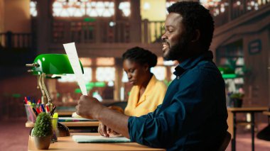 Üniversite öğrencisi kampüs kütüphanesinde ders çalışmak için çırpınıyor, bunalmış bir öğrenci endişeyle öğrenmeye çalışıyor. Erkek ergen notlarıyla ilgileniyor. Kamera B.