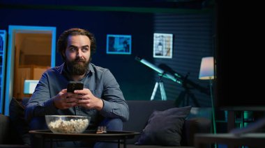 Adam evinde kanepede oturmuş akıllı telefondan arkadaşına mesaj atıyor ve onu televizyon kanalında film izlemeye davet ediyor. Evde cep telefonundan arkadaşıyla tartışan, TV şovu tavsiye eden, kamera B