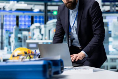 Resmi bir giysi mühendisi, yenilenebilir enerjinin geleceğinde teknik hassasiyet ve kurumsal stratejiyi temsil eden güneş paneli üretimini değerlendirdi. Montaj hattını denetler.