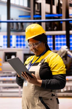 Sistem güncellemelerini gözden geçirmek ve ekipman bakımını denetlemek için tablet kullanan profesyonel endüstriyel teknisyen. Siyahi kadın mühendis imalat gelişmelerini sürdürmek için dijital çözümler üretiyor.