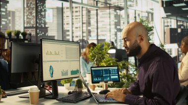 Ofisteki çalışanlar başarıyı kutlarken laptop ekranına bakıp başarılı sonuçlardan duydukları heyecanı dile getiriyorlar. Adam olumlu iş başarısından mutlu, kamera B