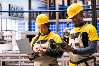 Endüstri 4.0 uzmanları gelişmiş otomatikleştirilmiş fabrikada dizüstü bilgisayar ve tablet kullanarak bakım bilgilerini topluyor. Yetenekli erkek ve kadın teknisyenler akıllı üretim tesislerinin optimizasyonunu denetliyor..